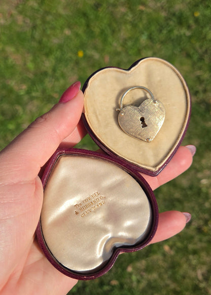 Heart-shaped jewelry box with a gold heart padlock pendant held by a hand against a grassy background